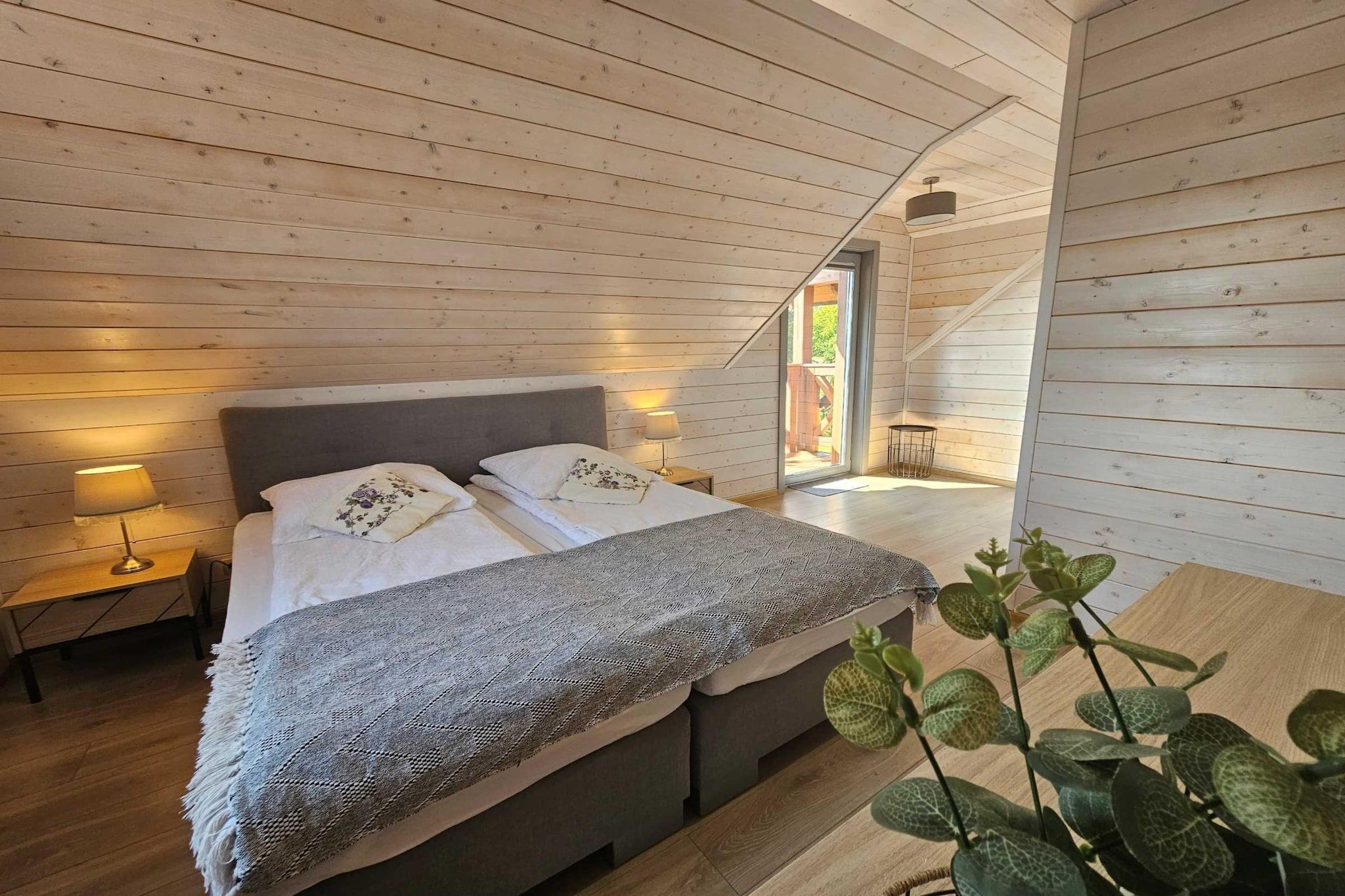 Un dormitorio de cabaña de madera con cama, lámparas de noche y vistas al exterior.