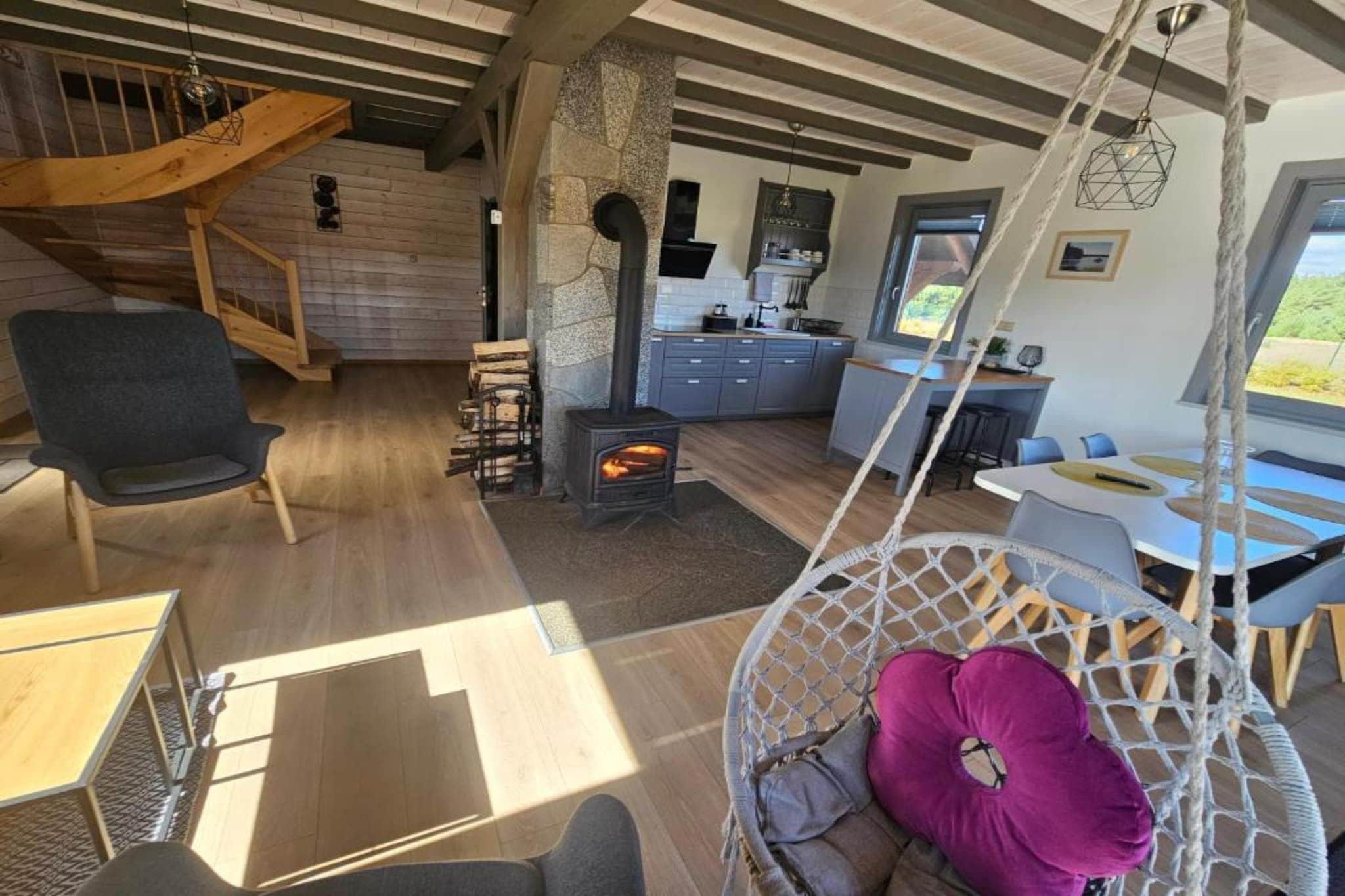 Een gezellig interieur met een stenen openhaard, houten balken, een hangstoel en een keukenhoek.