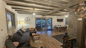 Un saló modern amb un sofà modular, una zona de menjador amb taula i cadires, una llar de foc i un gran finestral amb vistes a l'exterior.