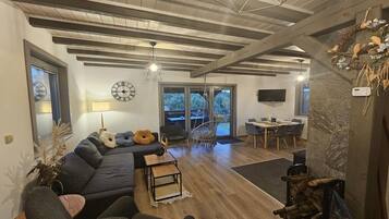 Una sala moderna con un sofá oscuro, una mesa de centro y un comedor con televisor.