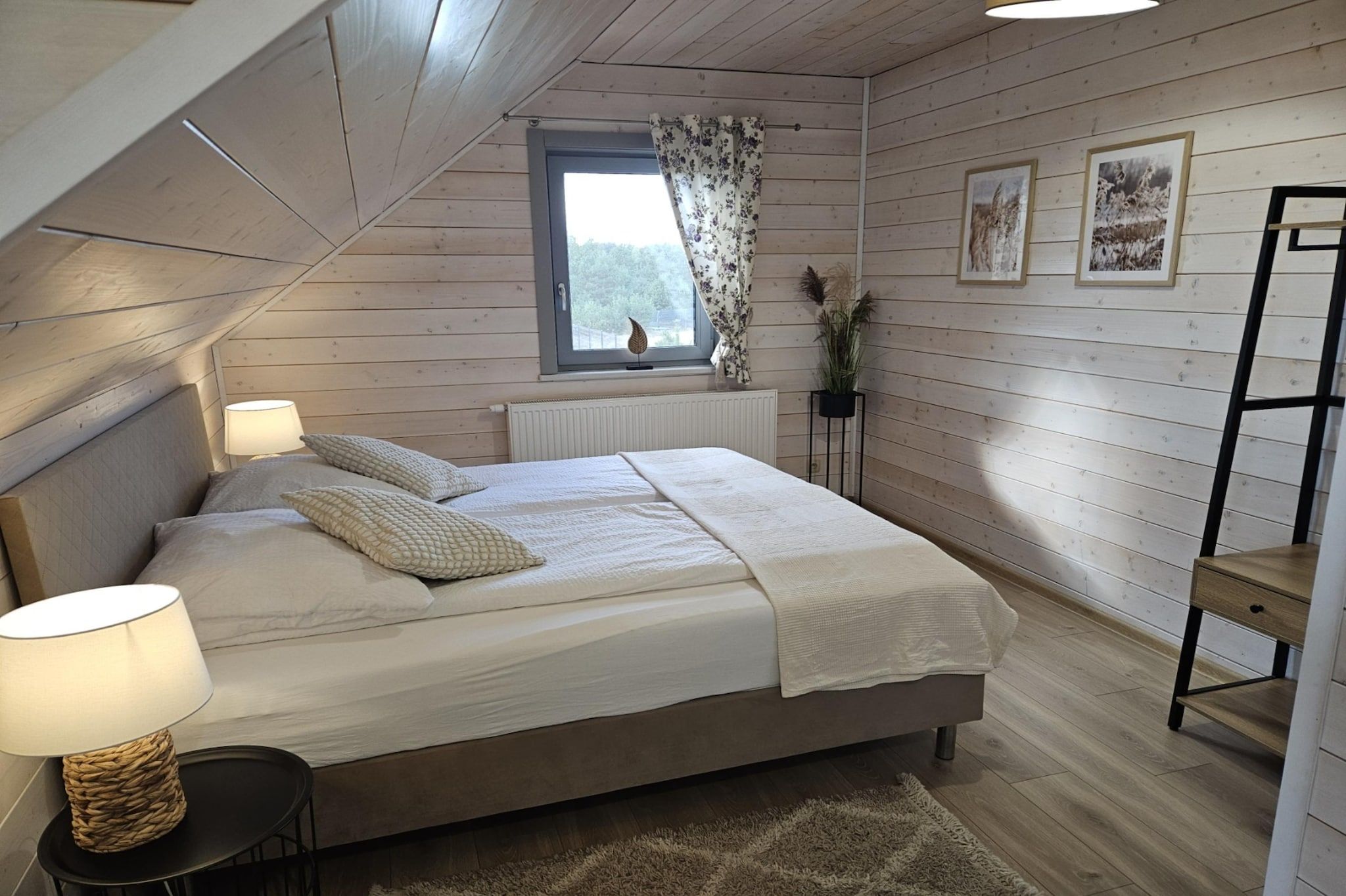 Une chambre à coucher avec un lit, des lampes de chevet, une fenêtre avec des rideaux, un radiateur et une plante.