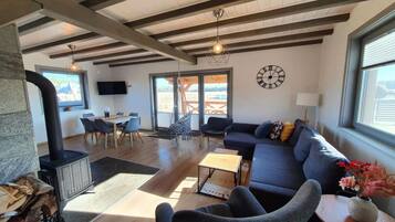 A spacious living room with a stone fireplace, a large sofa, and a television mounted on the wall.