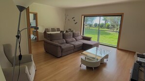 Una sala de estar moderna con un sofá modular, una mesa de centro de vidrio y un ventanal con vistas a un paisaje verde.