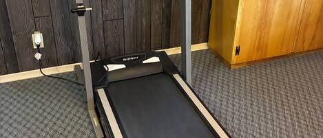 A treadmill in a room with a wooden cabinet and a carpeted floor.