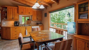 Cocina de madera con un gran ventanal, una mesa de comedor y sillas de mimbre.