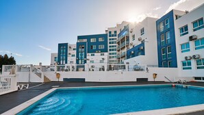 Ein modernes Hotel mit Dachpool, mehreren Balkonen und blauem Himmel.