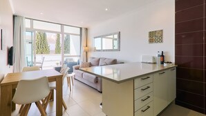 Eine moderne Küche mit einer zentralen Kochinsel, einem Essbereich mit Holztisch und Stühlen, einer Couch und einem großen Fenster, das für natürliches Licht sorgt.
