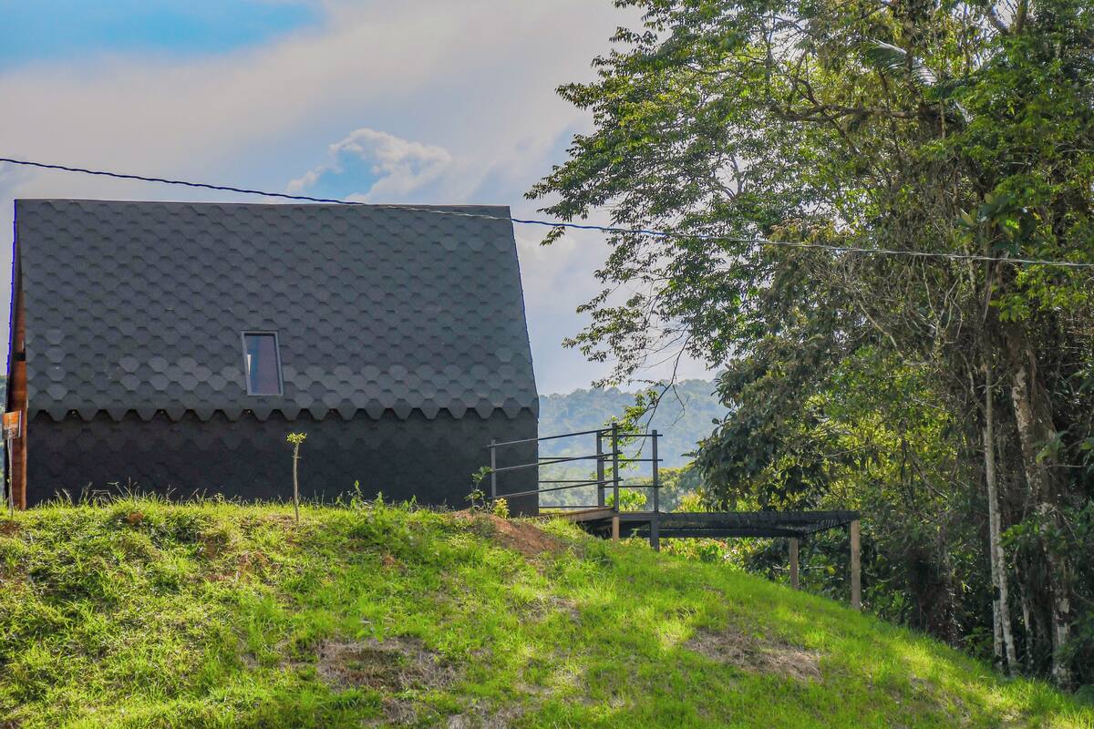 A building with a tiled roof and a small window, surrounded by greenery and a hilly landscape.