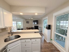 A modern kitchen with granite countertops, white cabinetry, a built-in sink, and a large window offering a view of the outdoors. - Sunset Point Lakeview Home Near Margaritaville (Osage Beach)