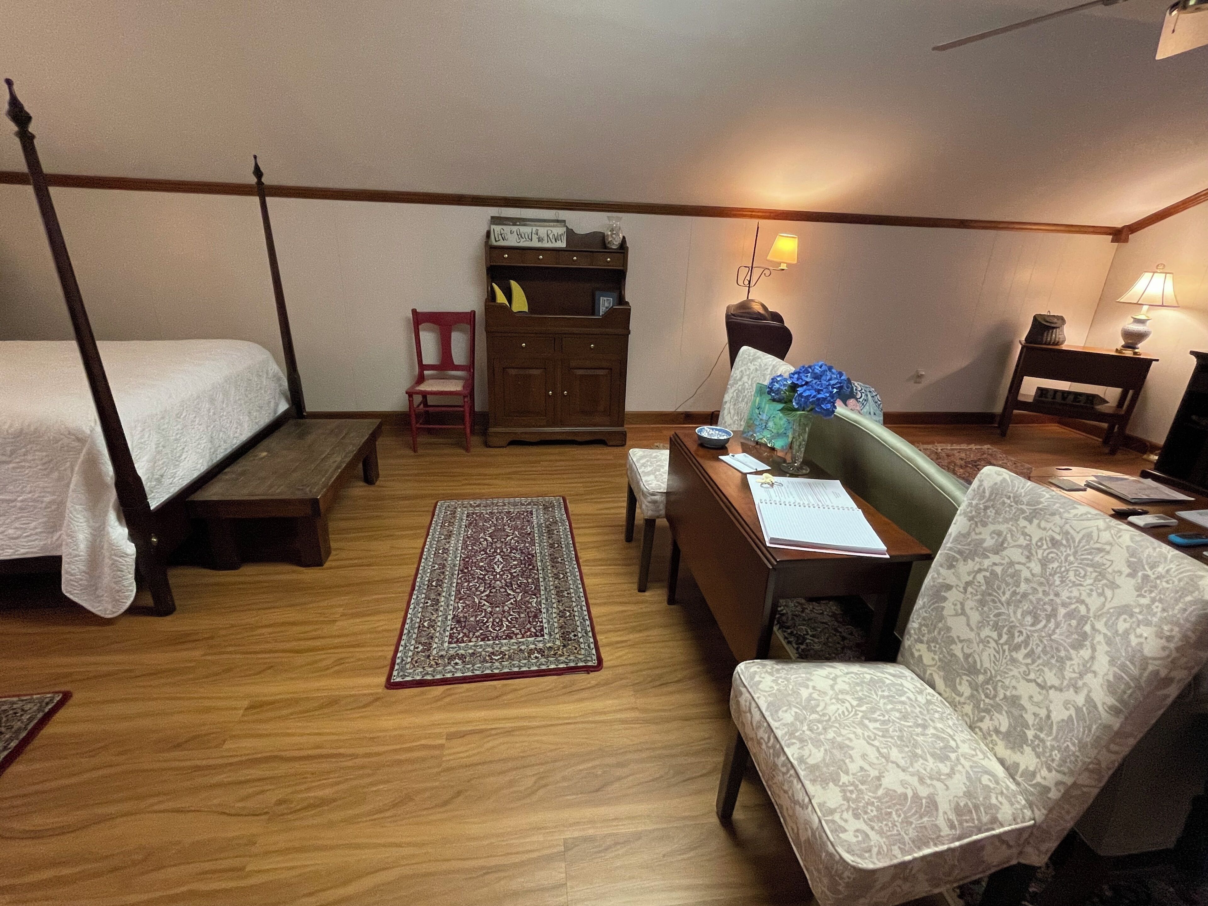Un dormitorio con cama con dosel, un escritorio con silla, una mesita con lámpara y una silla roja.