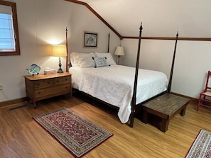A bedroom with a four-poster bed, wooden nightstand, bedside lamps, a framed picture on the wall, and a red and gray patterned rug. - Waterfront loft with beautiful views of the Perquimans River from Sunset Loft! (Hertford)