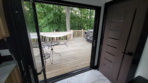 A wooden deck with a table and chairs, a grill, and a view of trees.