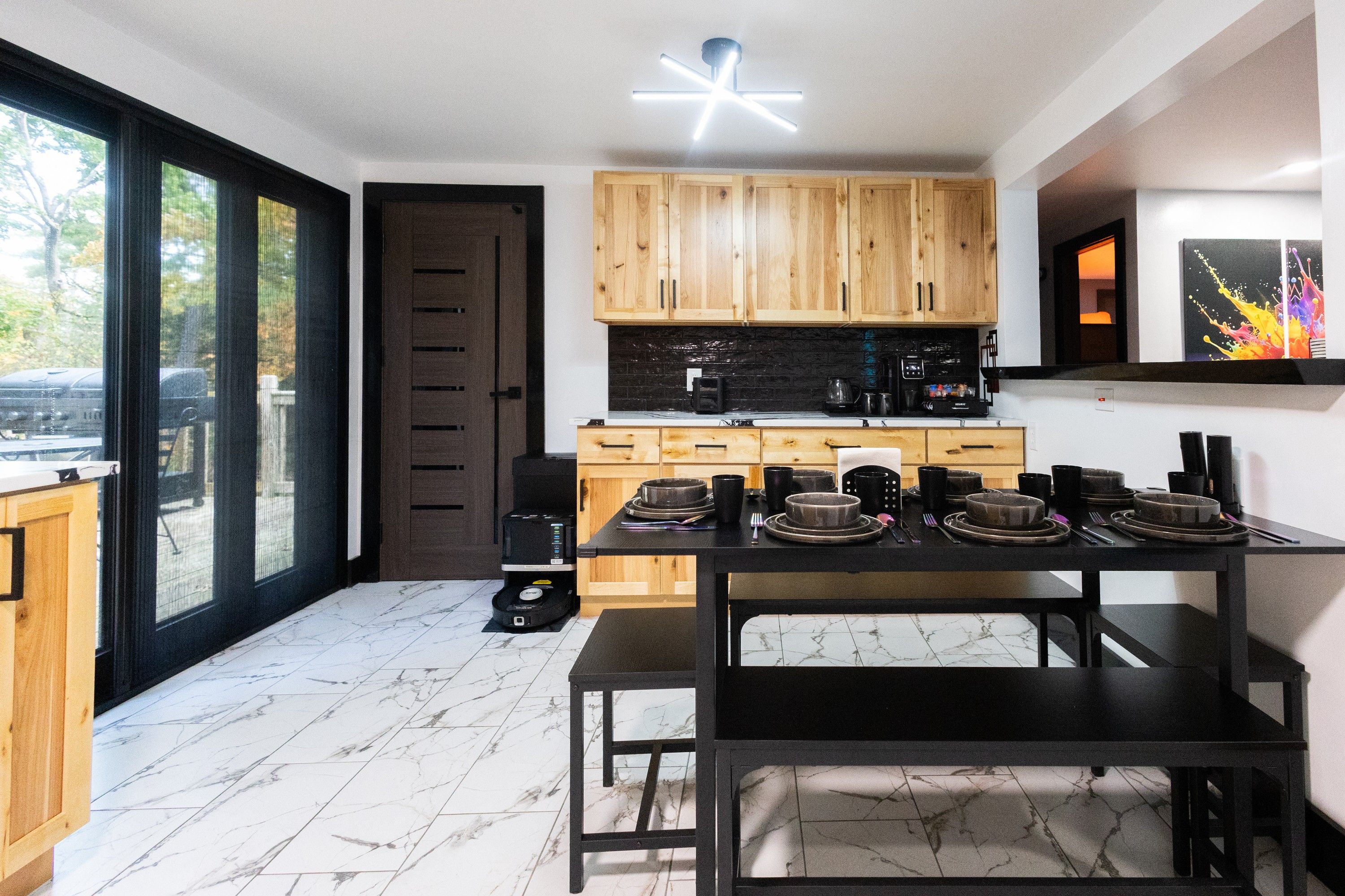 A modern kitchen with wooden cabinets, a black countertop, and a dining area with a black table and chairs.