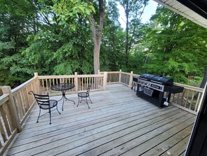 Une terrasse en bois avec un barbecue, deux tables en métal et des chaises.