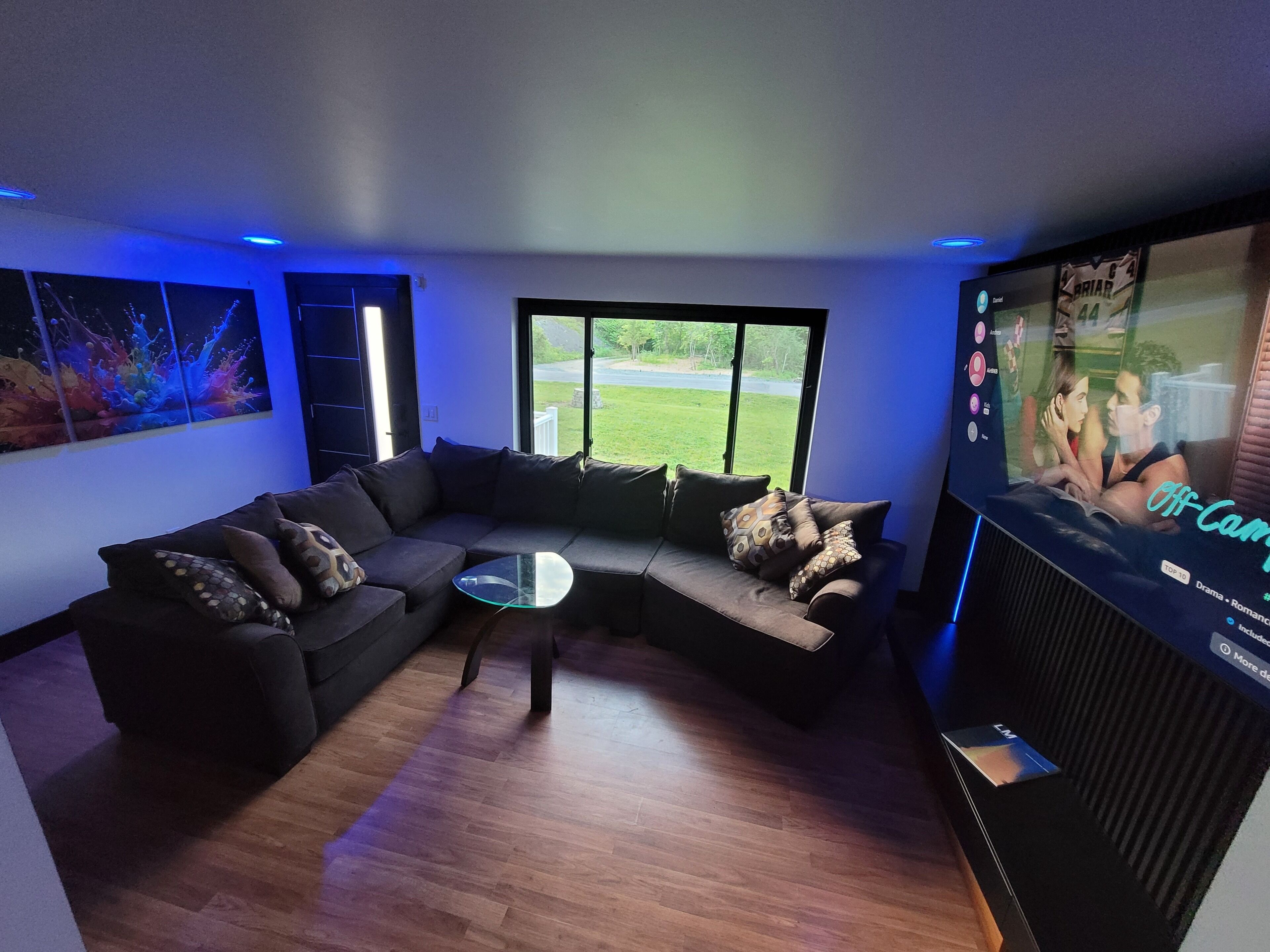 Una sala de estar moderna con un sofá modular, una mesa de centro de vidrio y una gran pantalla de televisión que muestra una película.