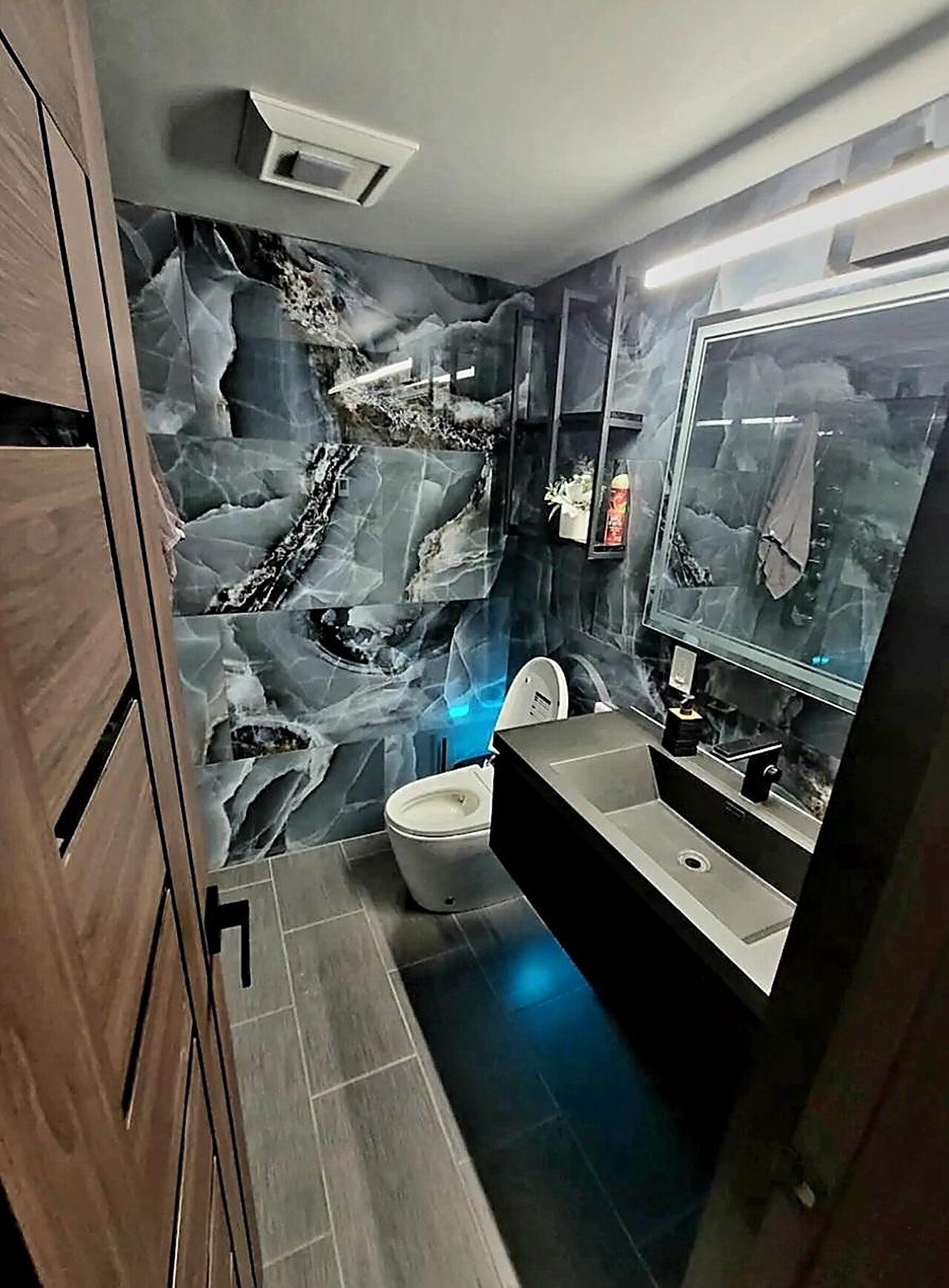 A modern bathroom with a marble backsplash, a toilet, a sink, and a mirror.
