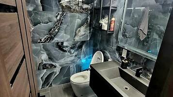 A modern bathroom with a marble backsplash, a toilet, a sink, and a mirror.