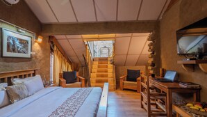 A bedroom with a bed, a desk with a laptop, a TV, and a staircase leading to a balcony. - The Divine Hima (Dharamshala)