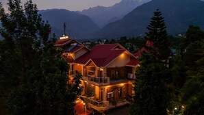 A multi-story building with a red roof, surrounded by trees and mountains in the background. - The Divine Hima (Dharamshala)