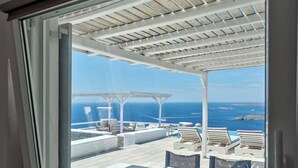 Un balcón con vista al océano, muebles blancos para exteriores y una estructura de pérgola.
