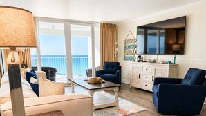 Ein Wohnzimmer mit Sofa, Sesseln, Couchtisch und einem an der Wand befestigten Fernseher.