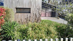 Un edificio moderno con fachada de madera, una ventana y un jardín con diversas plantas.