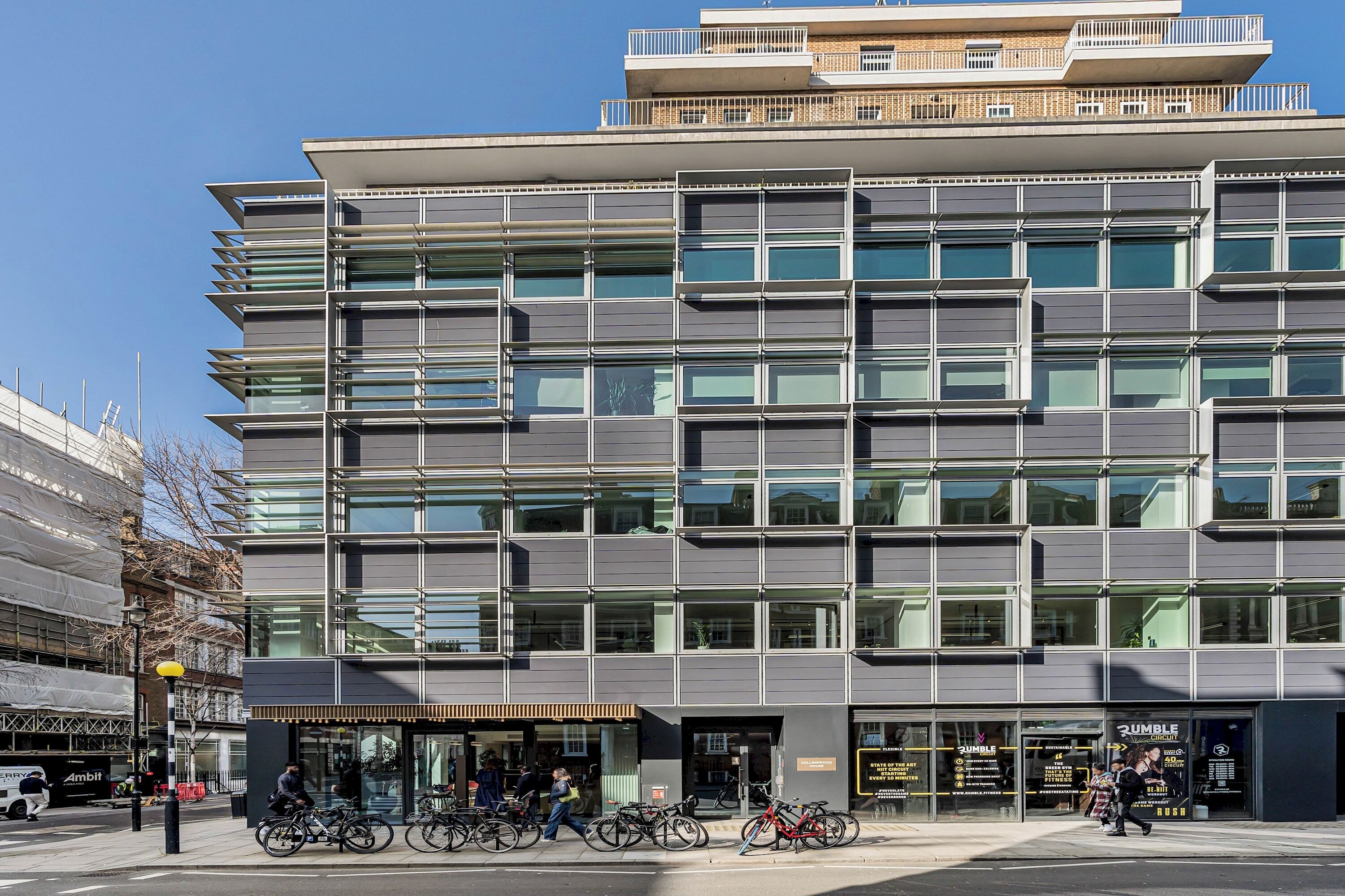 En moderne bygning med flere etager, store vinduer og en indgang i stueplan, hvor cykler er parkeret udenfor.