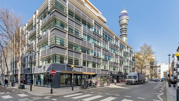 Un bâtiment moderne à plusieurs étages, doté d’une entrée imposante, de grandes fenêtres et d’une tour visible en arrière-plan.
