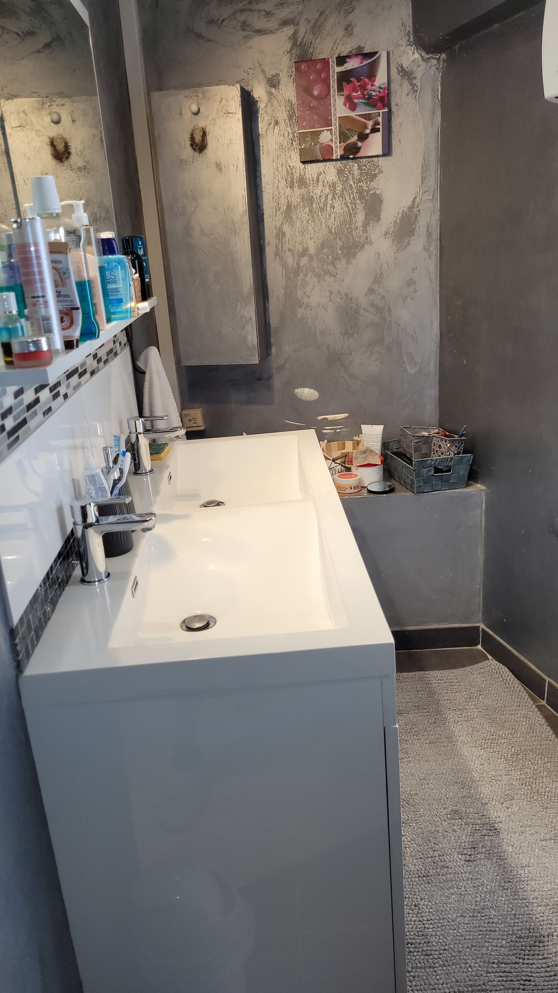 Une salle de bain avec un lavabo blanc, un miroir et une étagère contenant des articles de toilette.