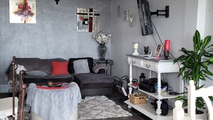 Ett modernt vardagsrum med en grå soffa, ett soffbord, en kristallkrona och ett vitt konsolbord med diverse föremål.