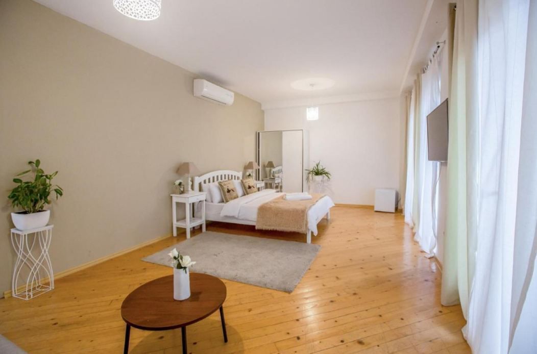 A bedroom with a bed, bedside tables, a mirror, a small table with a vase, and a potted plant.