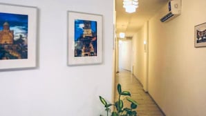 A hallway with framed pictures on the walls, a potted plant, and an air conditioning unit. - Boutique Hotel Meidan View (Tbilisi)