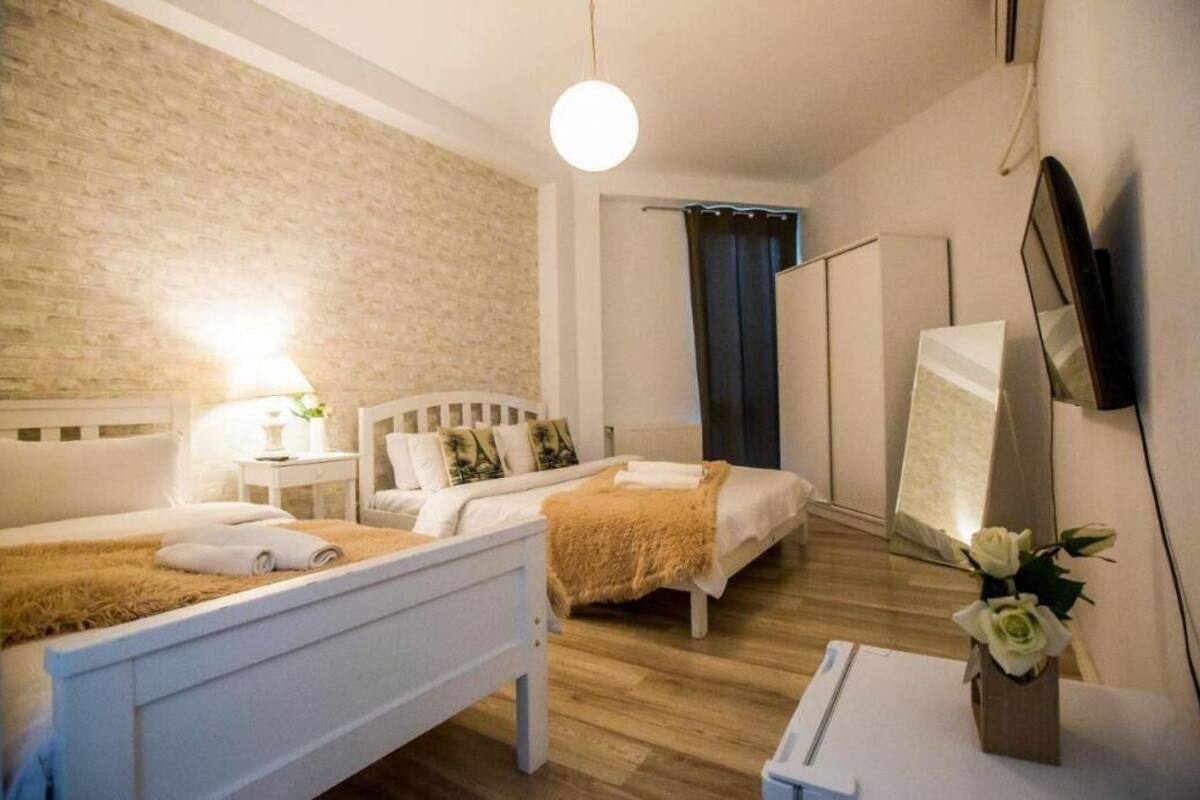 Une chambre avec deux lits, une table de chevet avec une lampe, un miroir et une petite table sur laquelle est posé un vase de fleurs.