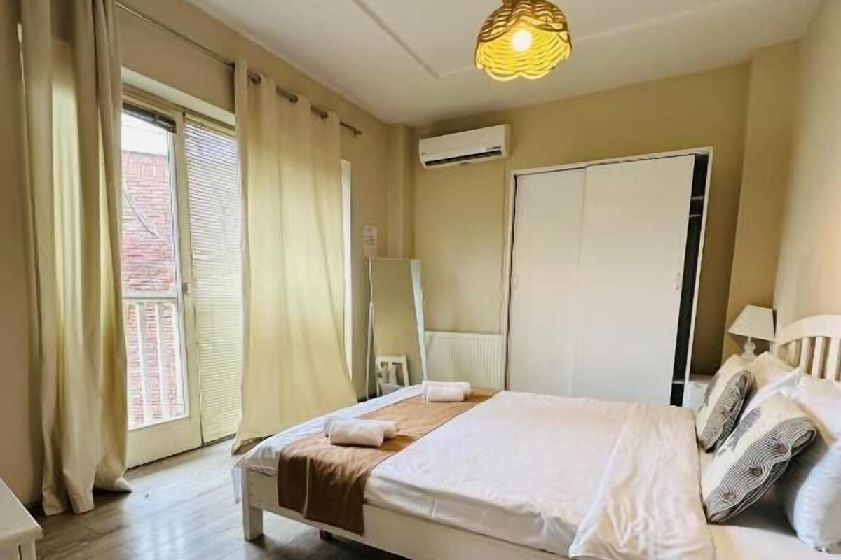 Une chambre à coucher avec un lit, une table de chevet, une lampe et une fenêtre avec des rideaux.