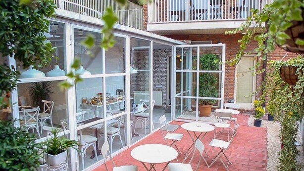 A glass-enclosed patio with white tables and chairs, a brick floor, and potted plants. - Boutique Hotel Meidan View (Tbilisi)