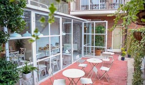 A glass-enclosed patio with white tables and chairs, a brick floor, and potted plants. - Boutique Hotel Meidan View (Tbilisi)