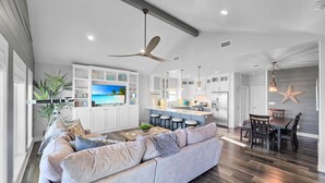 A spacious living area with a large gray sofa, a kitchen with white cabinets, and a dining area with a wooden table and chairs. - Seashell Shack on Shrimp, Sleeps 11 - 3 bedroom 2.5 Bath - Great View (Crystal Beach)