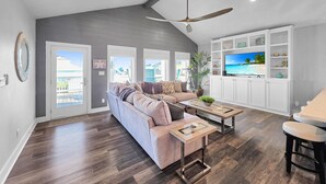 A spacious living room with a large sofa, coffee table, and TV. There are multiple windows and a ceiling fan. - Seashell Shack on Shrimp, Sleeps 11 - 3 bedroom 2.5 Bath - Great View (Crystal Beach)