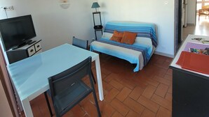 A small, furnished room with a bed, a desk, a chair, a television, and a lamp.