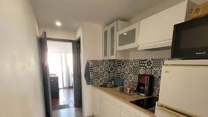 A narrow kitchen with white cabinets, a microwave, and a coffee maker.