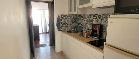 A narrow kitchen with white cabinets, a microwave, and a coffee maker.