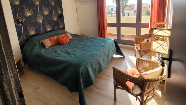 A bedroom with a bed, a chair, a window with curtains, and a wall with a leaf pattern.