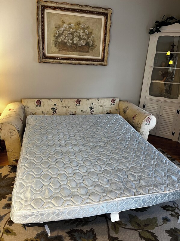 A bedroom with a bed, a floral-patterned sofa, a cabinet with glass doors, and a framed picture on the wall.