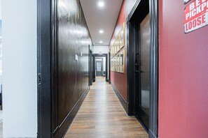 A hallway with wooden flooring, black doors, and a red wall with a 'Be Pick Up Loose' sign.