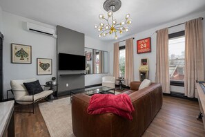 A modern living room with a sofa, armchairs, a TV, and a chandelier.
