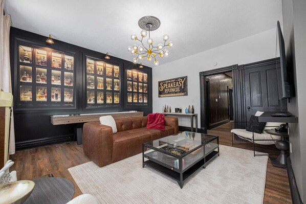 A modern living room with a brown leather sofa, a glass coffee table, and a large window display of liquor bottles.