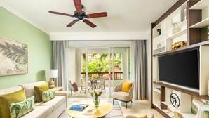 Uma sala de estar com sofá, poltronas, mesa de centro, televisão e varanda com mobiliário de exterior.