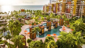 Resort com piscina central, vários edifícios e palmeiras.
