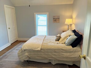 Une chambre à coucher avec un lit, une fenêtre avec des stores, une lampe et une porte.