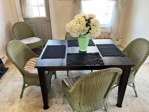 Une table à manger ornée d’un vase de fleurs, de sets de table noirs et de chaises en osier.